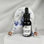 A black glass bottle sitting in front of a white and blue silk sachet pouch on a white background